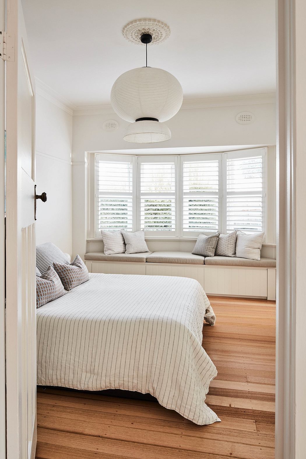 Cozy bedroom with built-in window seating, striped bedding, and modern light fixture.