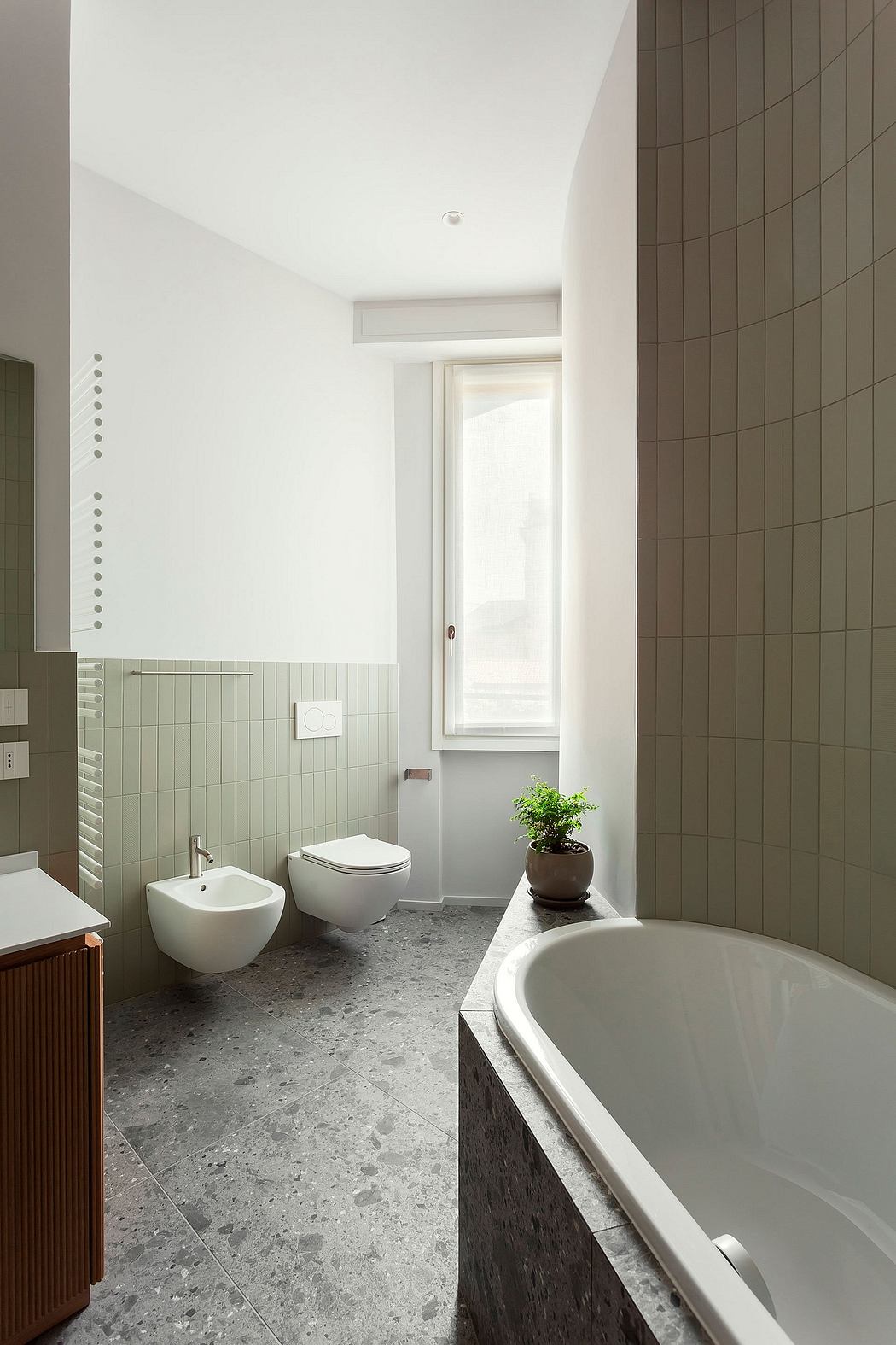 Modern, minimalist bathroom with white walls, grey tiled floor, freestanding bathtub, and potted plant.