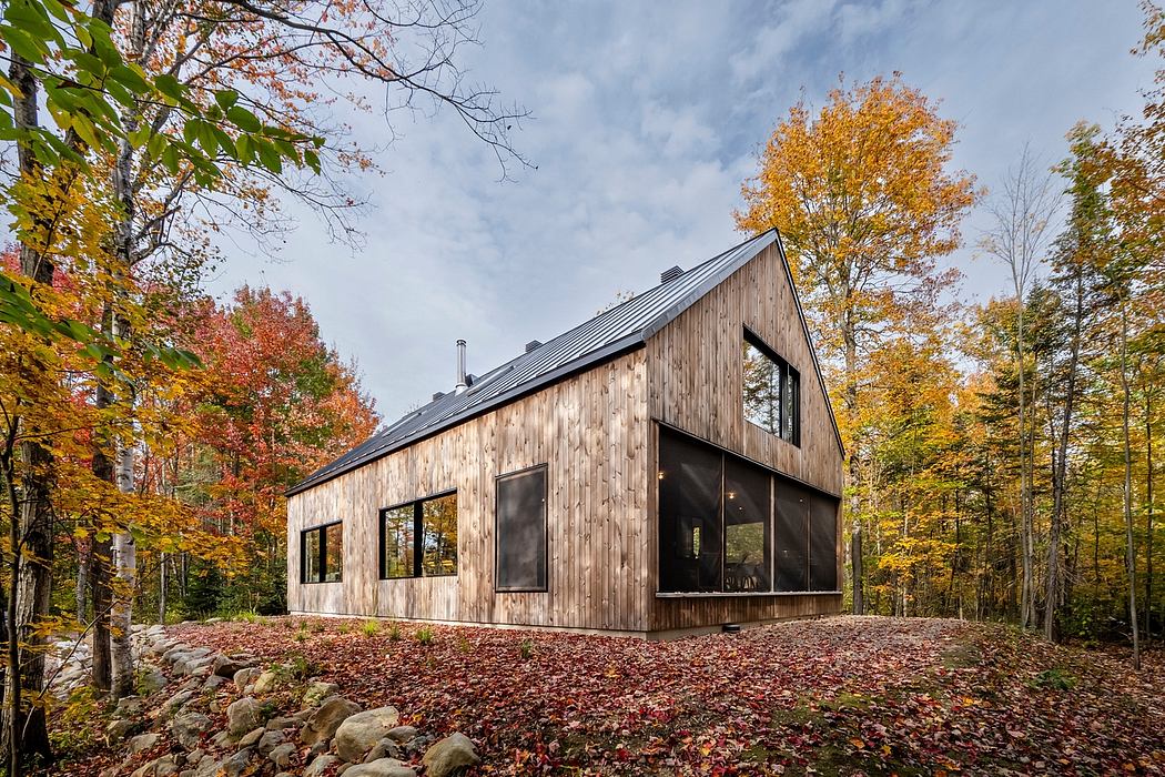 Modern A-frame cabin in a forest during autumn, with large windows and wooden exterior.
