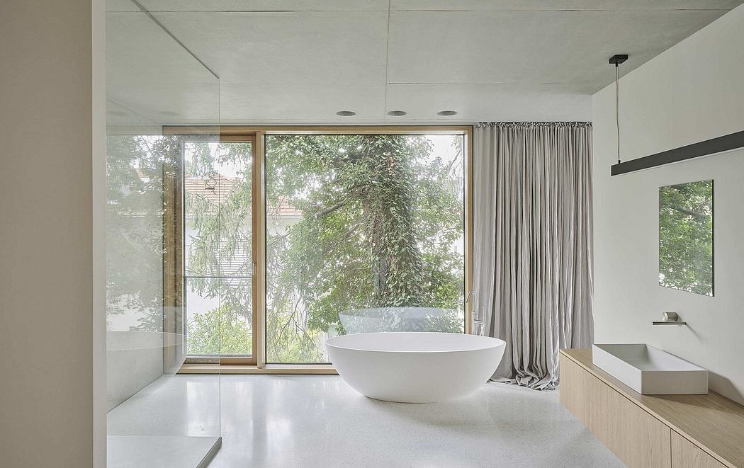 Modern bathroom with freestanding tub, curtained glass wall, and nature view.