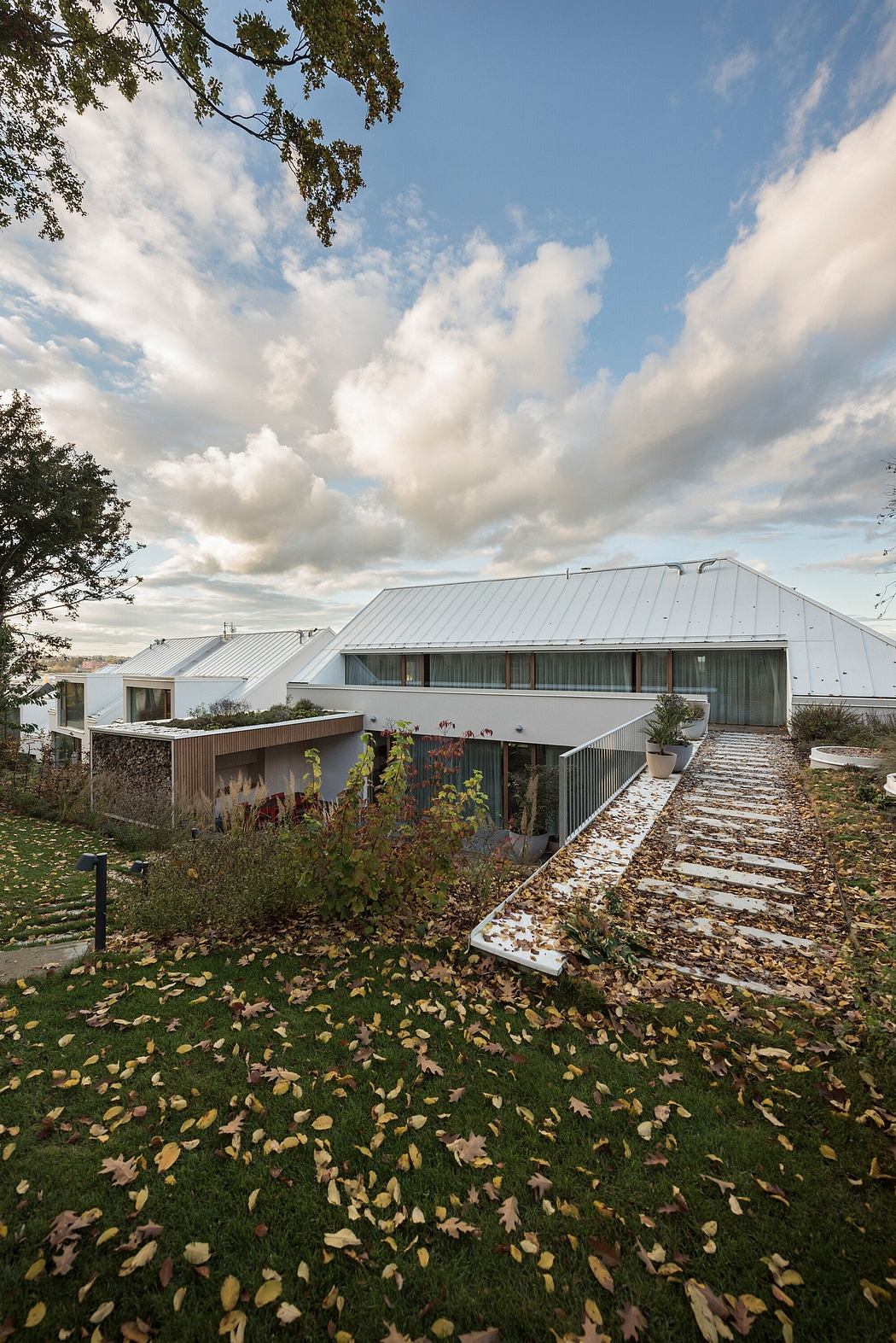Modern multi-level structure with metal roofing, wooden accents, and pathways amidst autumn leaves.