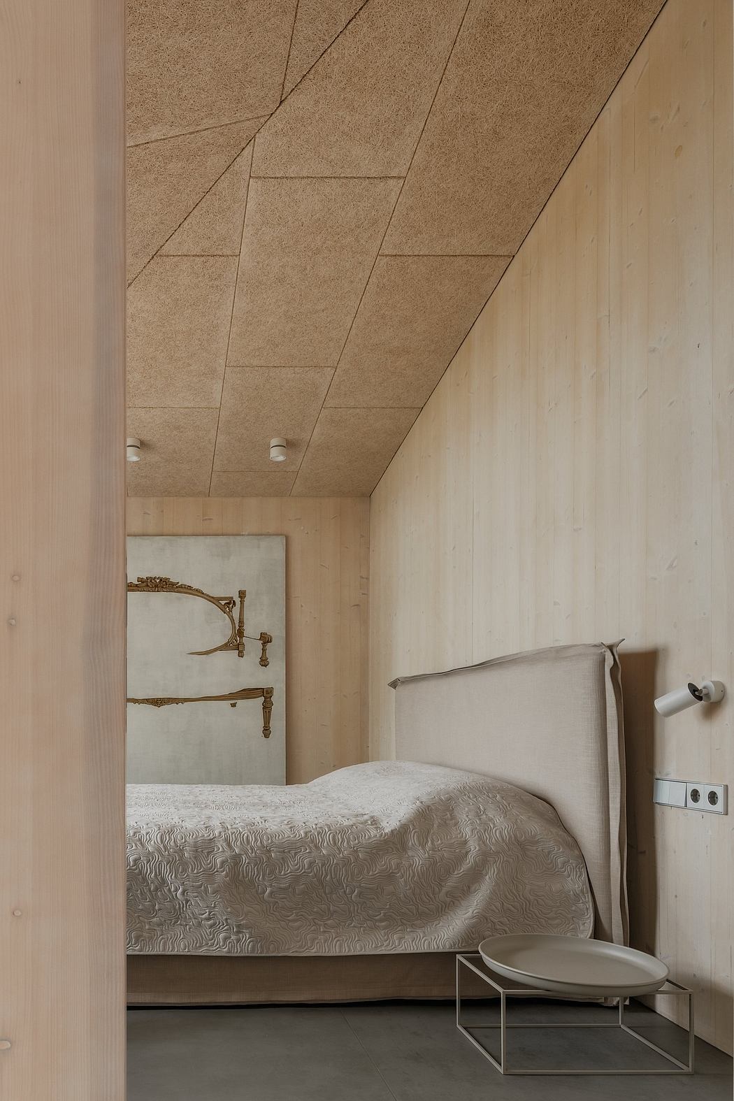 A cozy bedroom with a rustic wooden ceiling, a plush bed, and minimalist furniture.