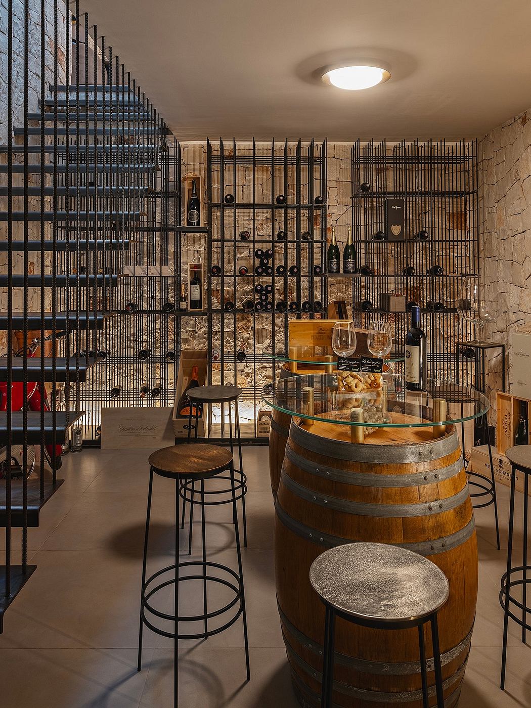 Rustic wine cellar with metal caged shelving, wooden barrels, and a glass-topped table.