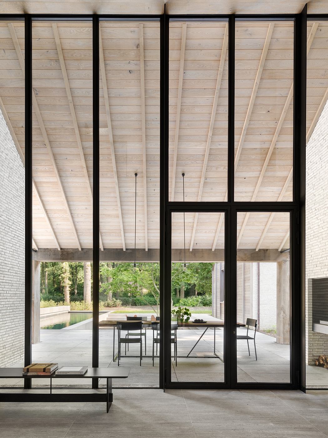 Striking wooden ceiling beams, expansive glass walls frame verdant outdoor view.