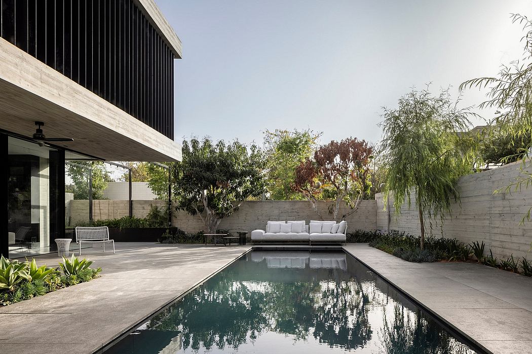 Minimalist outdoor patio with sleek black wooden building, pool, and lush vegetation.