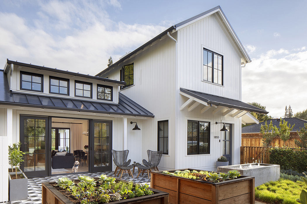 Modern farmhouse-style home with white siding, metal roof, and porch surrounded by lush landscaping.