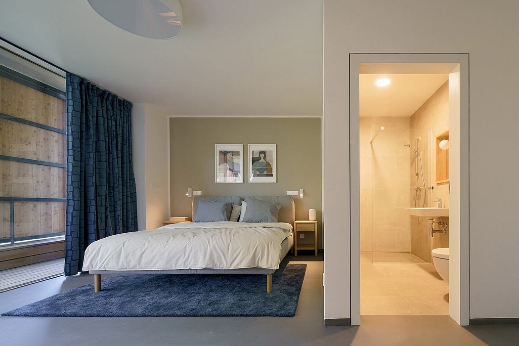 A cozy bedroom with gray walls, a plush rug, and an open bathroom door leading to a modern, well-lit interior.