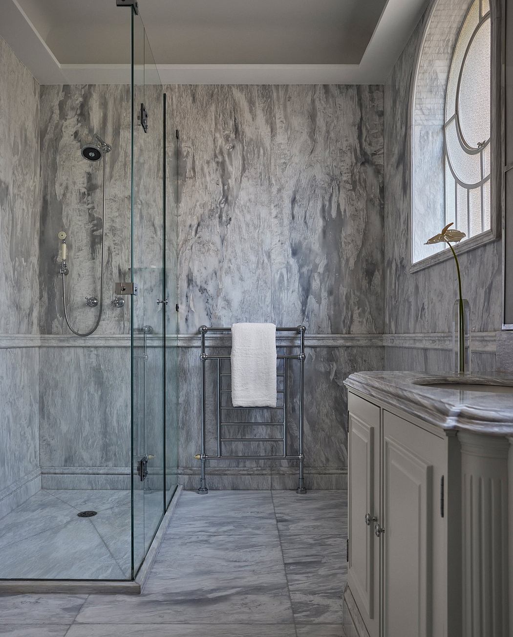 A sophisticated bathroom design with marble-patterned walls, glass shower, and towel rack.
