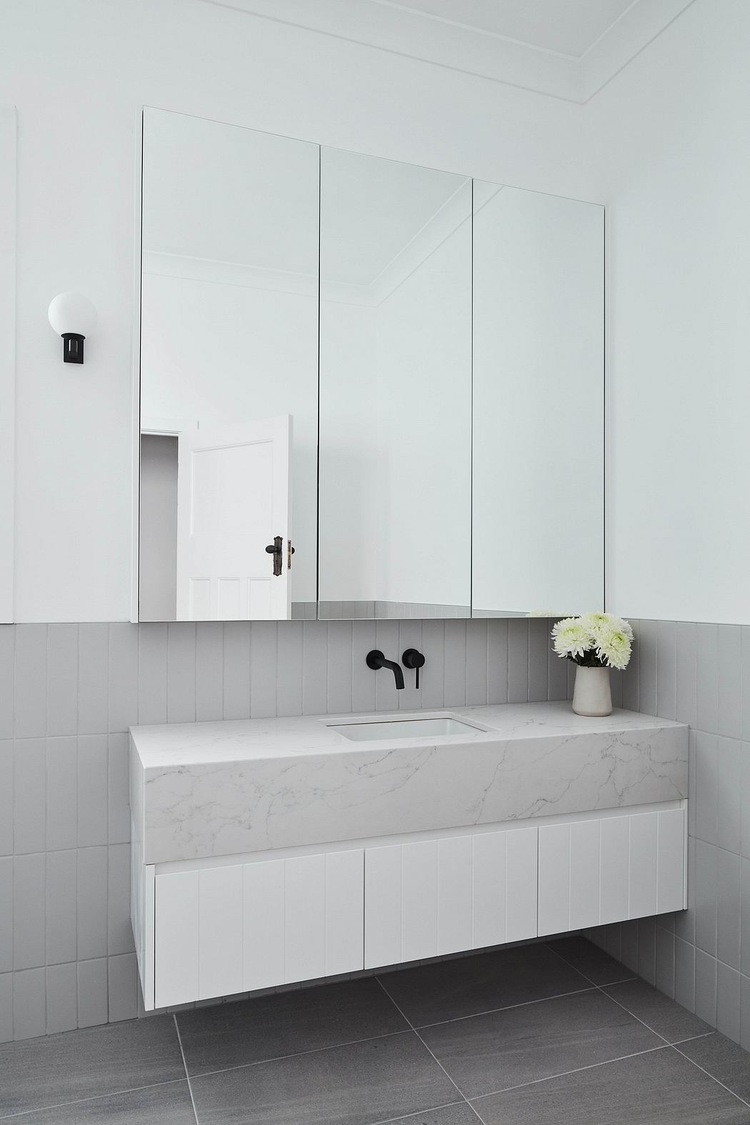A modern bathroom design with a white marble countertop, black fixtures, and recessed mirrors.