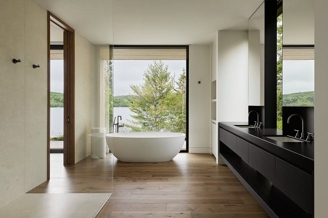 Spacious modern bathroom with freestanding tub, black vanity, and scenic woodland view.