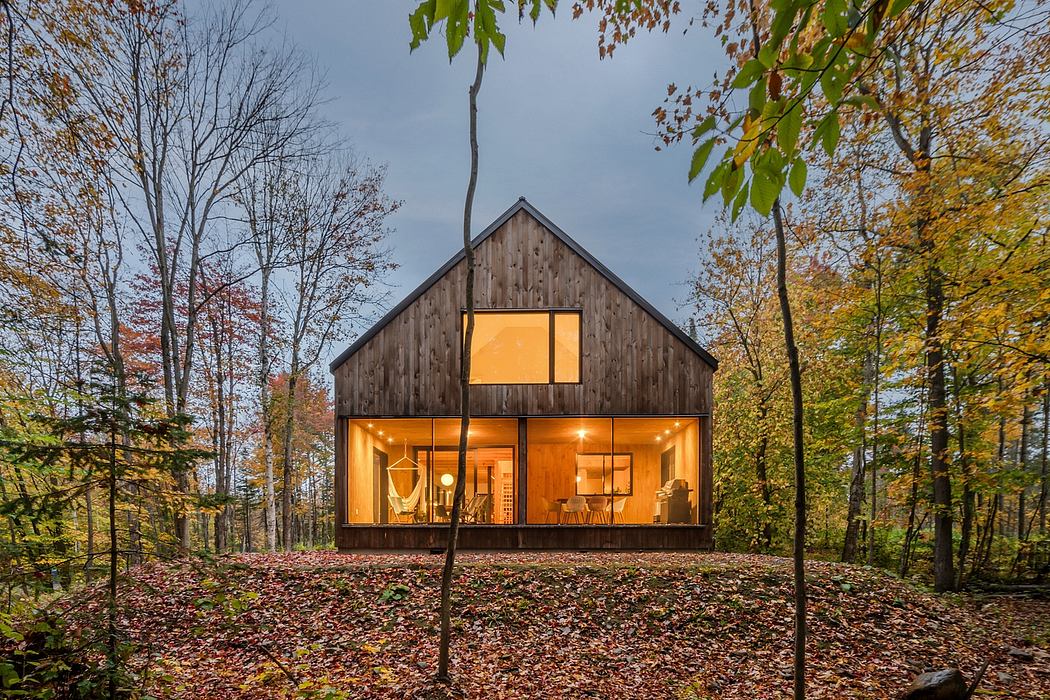 A cozy wooden cabin nestled in an autumn forest, illuminated by warm interior lighting.
