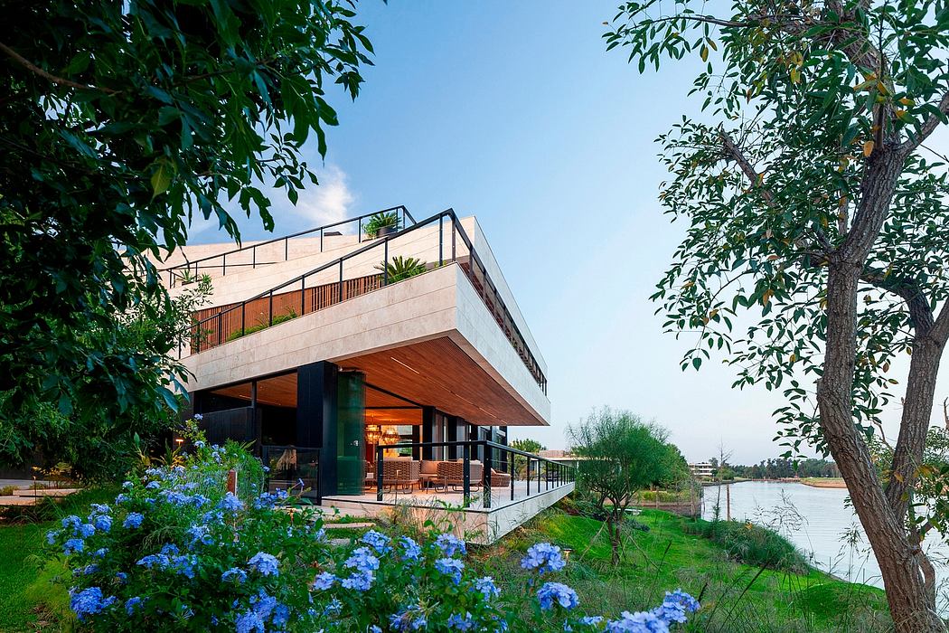 Modern lakeside home with cantilevered balcony, glass walls, and lush landscaping.