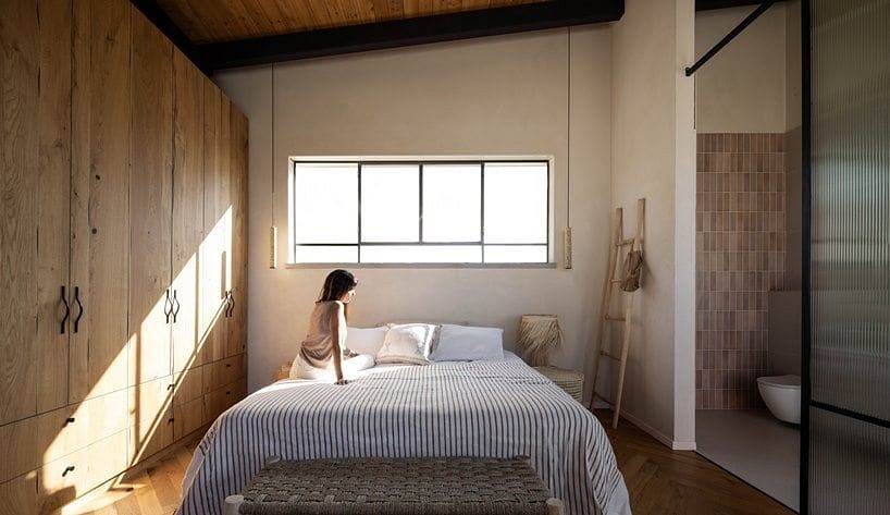 Cozy bedroom with wooden walls, large window, and minimal modern decor.