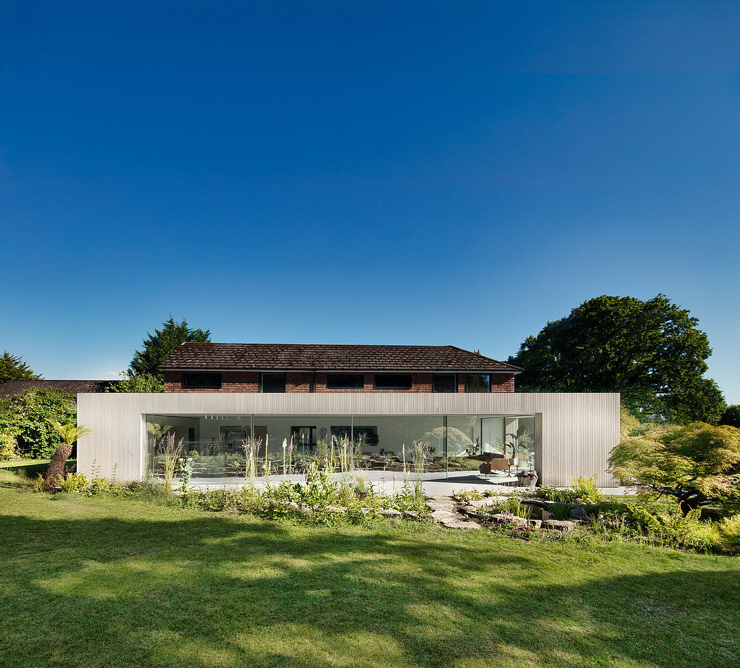 A modern glass-walled home with a traditional wooden structure above, surrounded by lush greenery.
