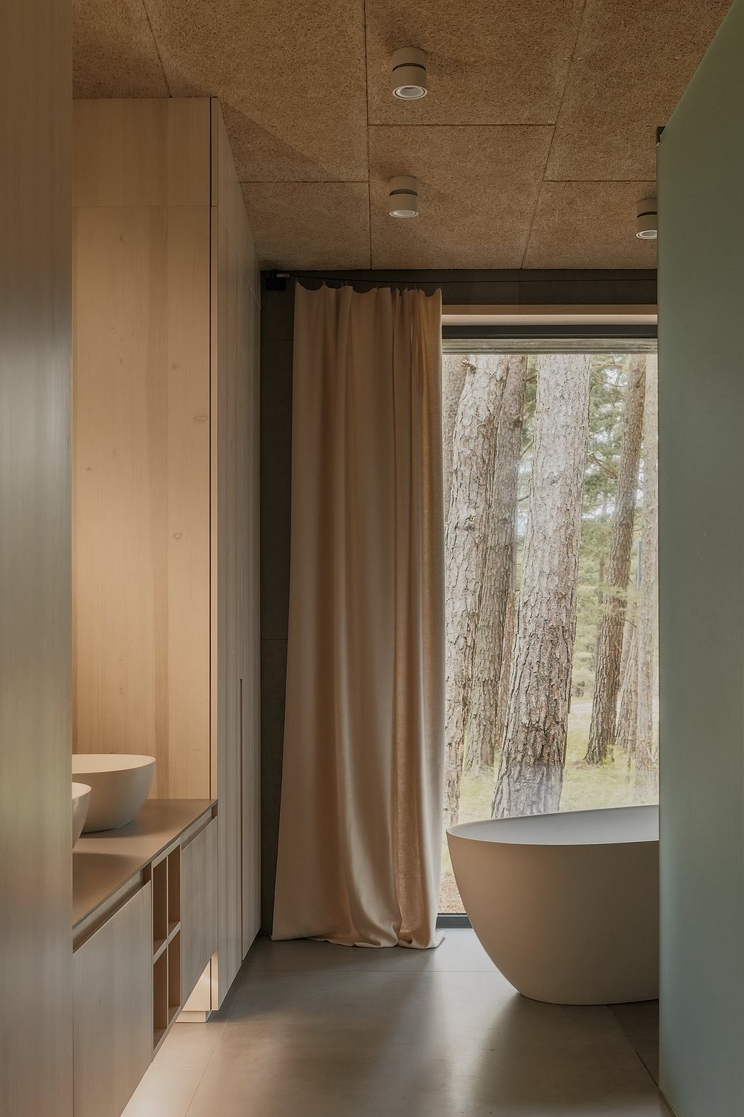 Cozy bathroom with wooden panels, freestanding tub, and scenic forest view through window.