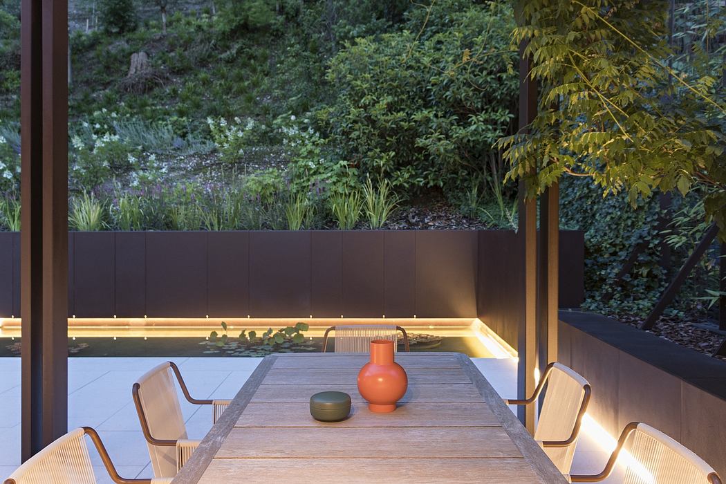 A cozy outdoor dining area with a wooden table, modern lighting, and a lush greenery backdrop.