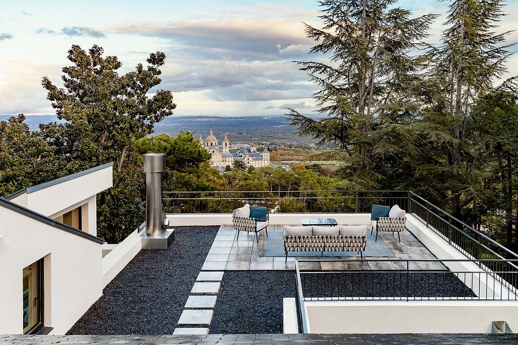 Modern patio with sleek furniture overlooking picturesque town and mountains.