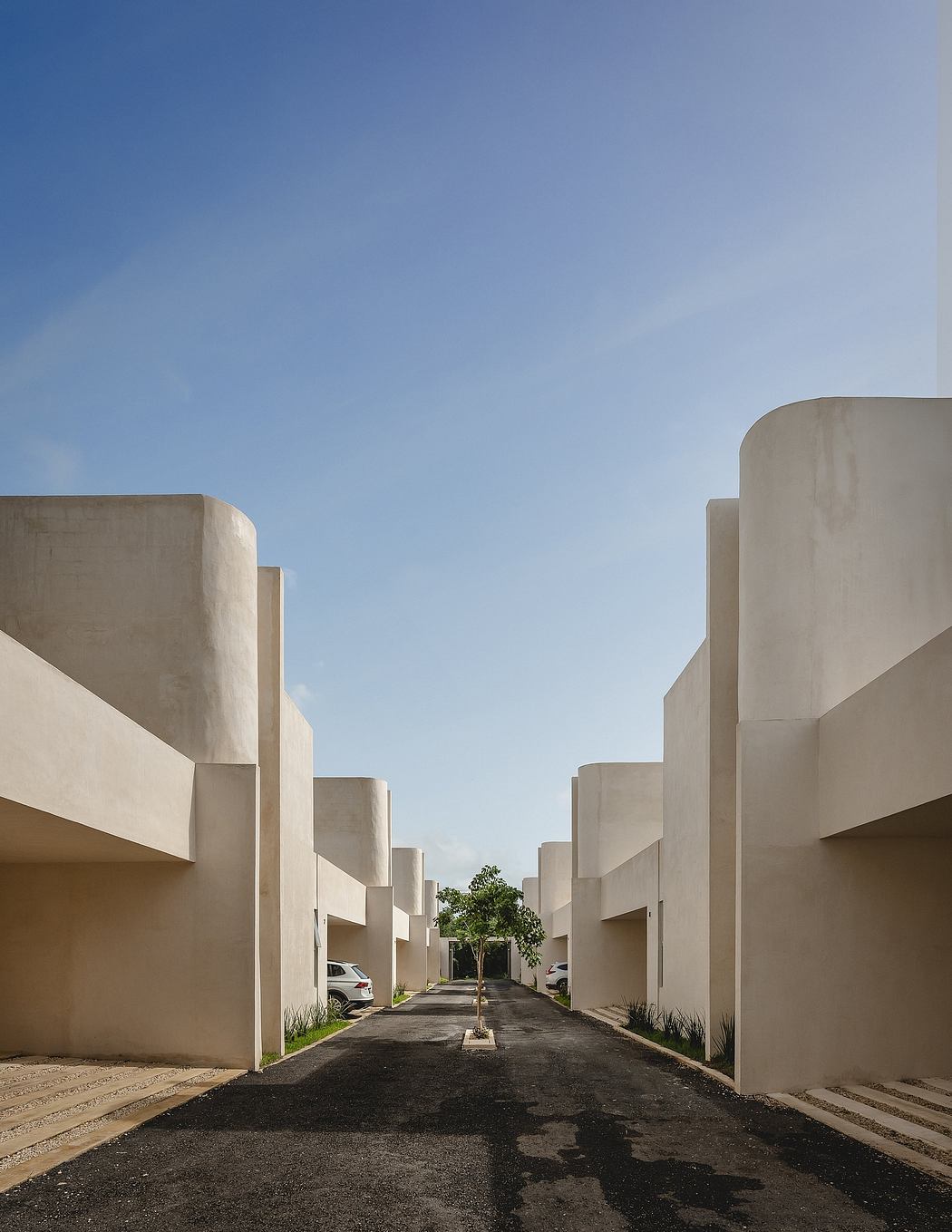 Minimalist architectural design featuring symmetrical concrete structures and a lone tree.