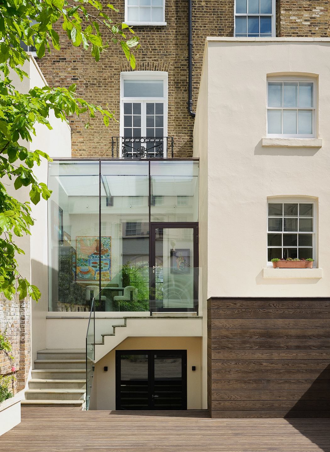 Modern glass entryway with wooden stairs and balcony, set against a brick facade.