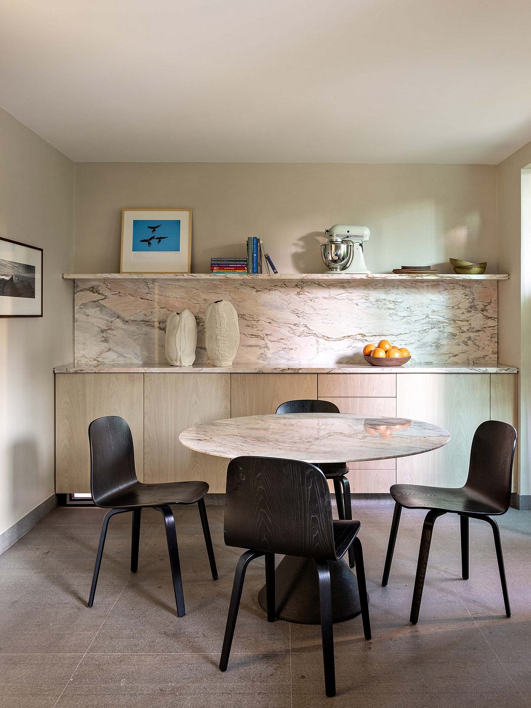 Modern kitchen with sleek marble countertop, minimalist wood cabinets, and round dining table.