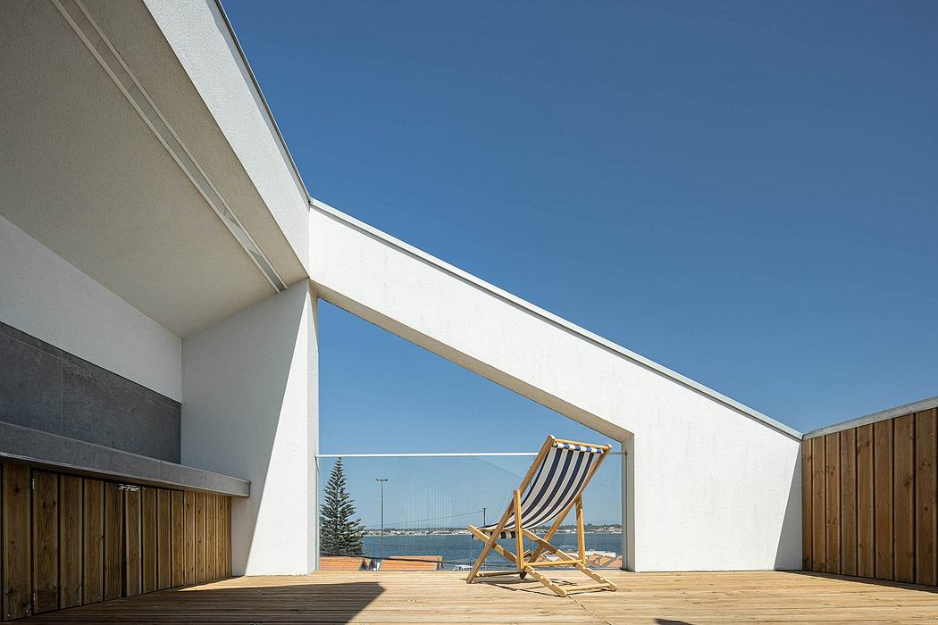 A modern architectural structure with a wooden deck, glass walls, and a lounge chair offering a scenic view.