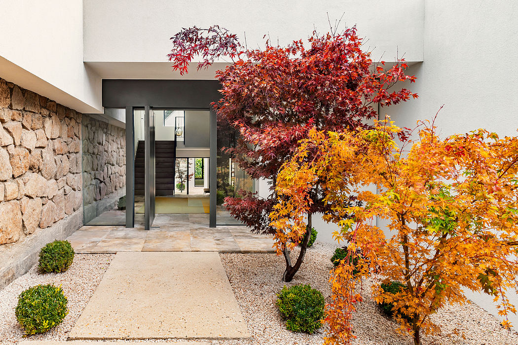 Modern home exterior with stone facade, glass entryway, and vibrant fall foliage.