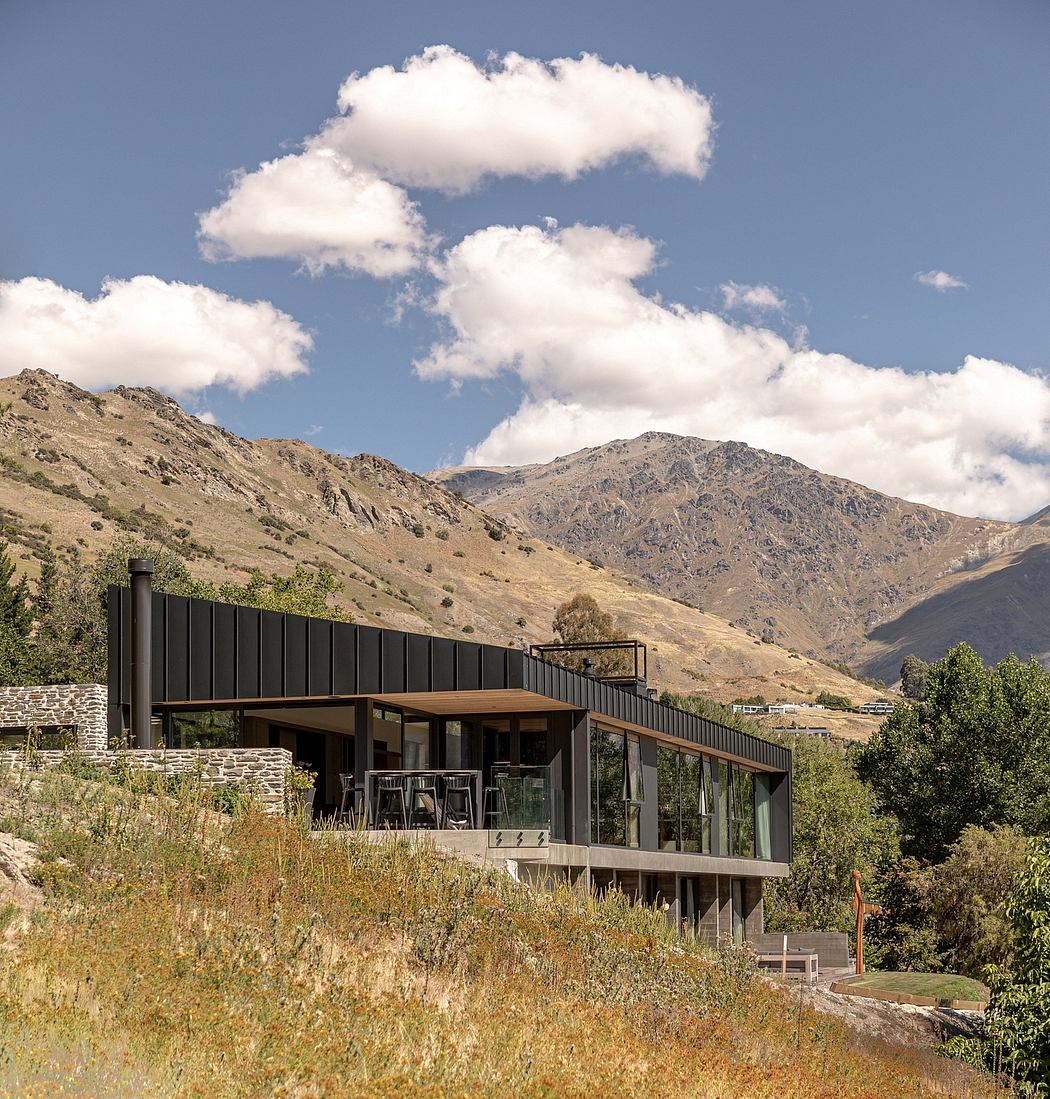 A modern mountain lodge with a glass facade and wooden accents nestled amidst rugged terrain.