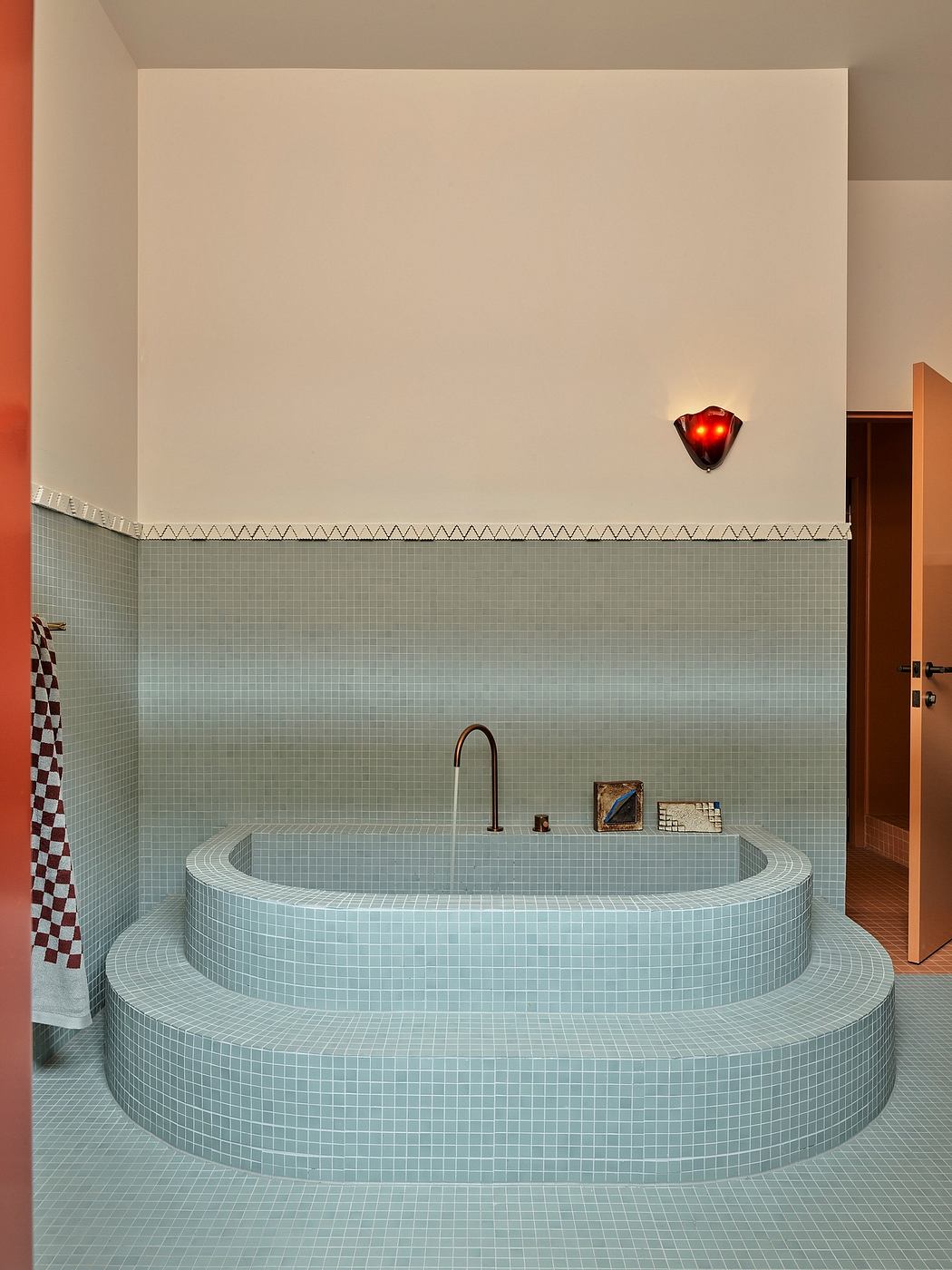 A modern bathroom with a sunken tub surrounded by grey mosaic tiles and a red light fixture.