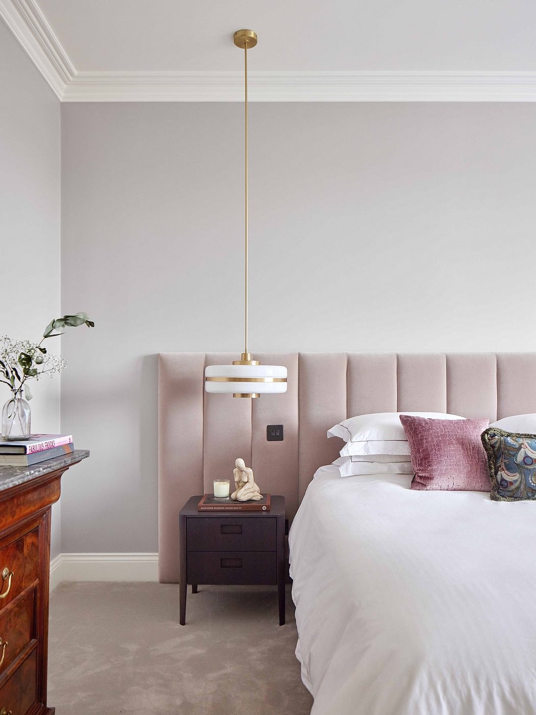 A cozy bedroom with a plush pink bed frame, a pendant light, and a wooden nightstand.