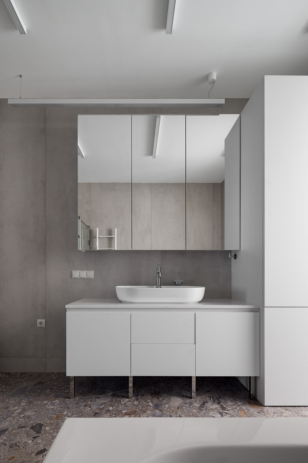 A minimalist bathroom design with a white vanity, vessel sink, and recessed storage cabinets.