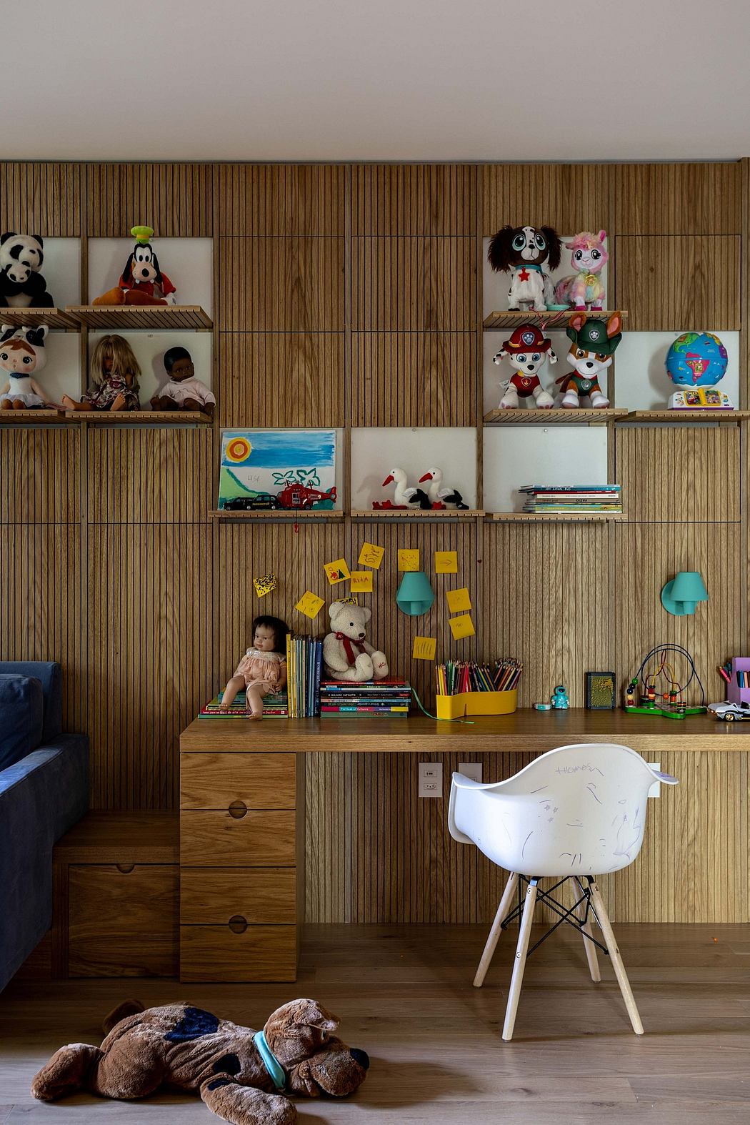 A cozy, well-designed children's room with wooden shelving, colorful toys, and a white Eames-style chair.