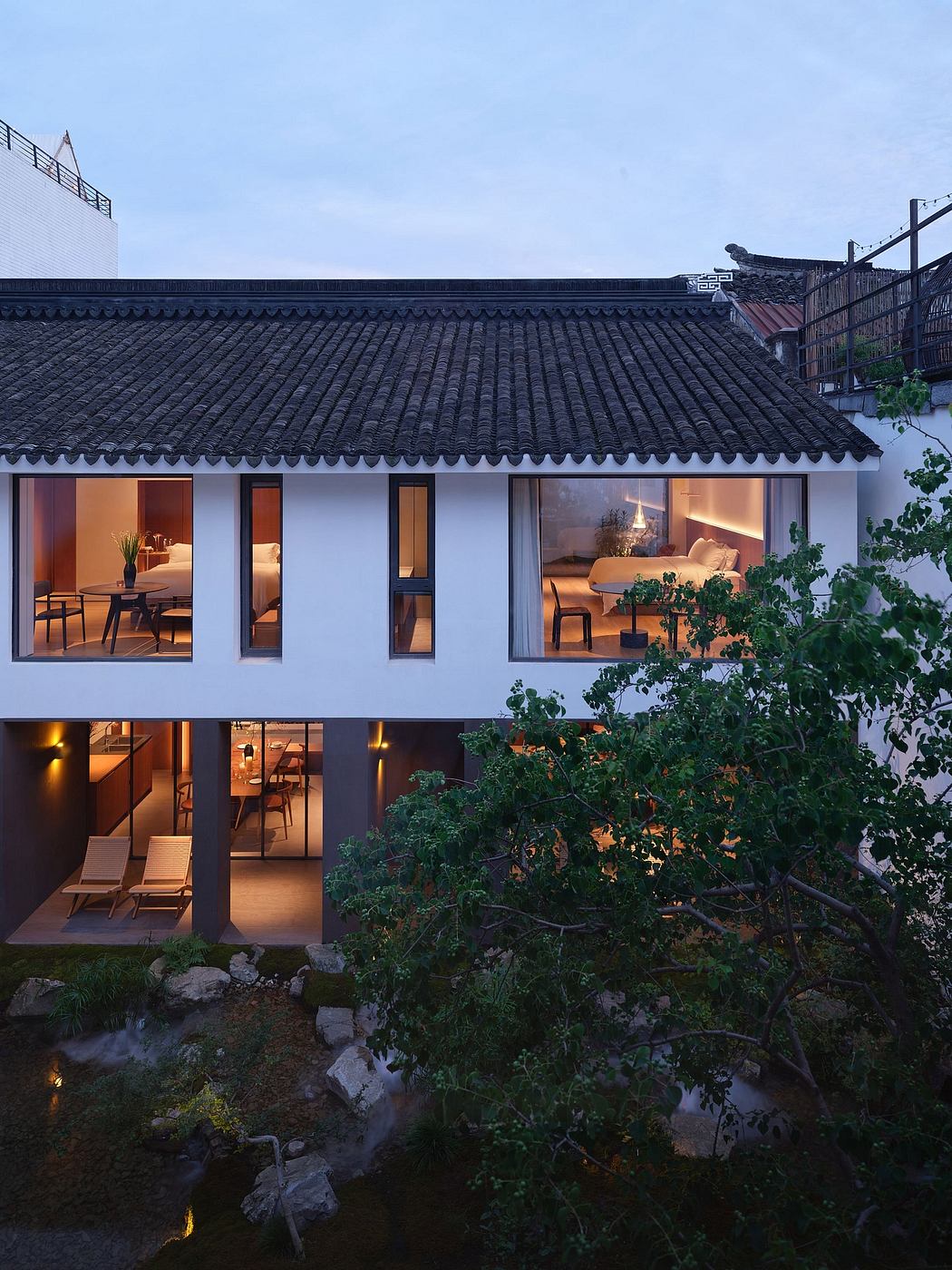 The image shows a modern Asian-style building with a traditional tiled roof, large windows, and a cozy interior with furniture.