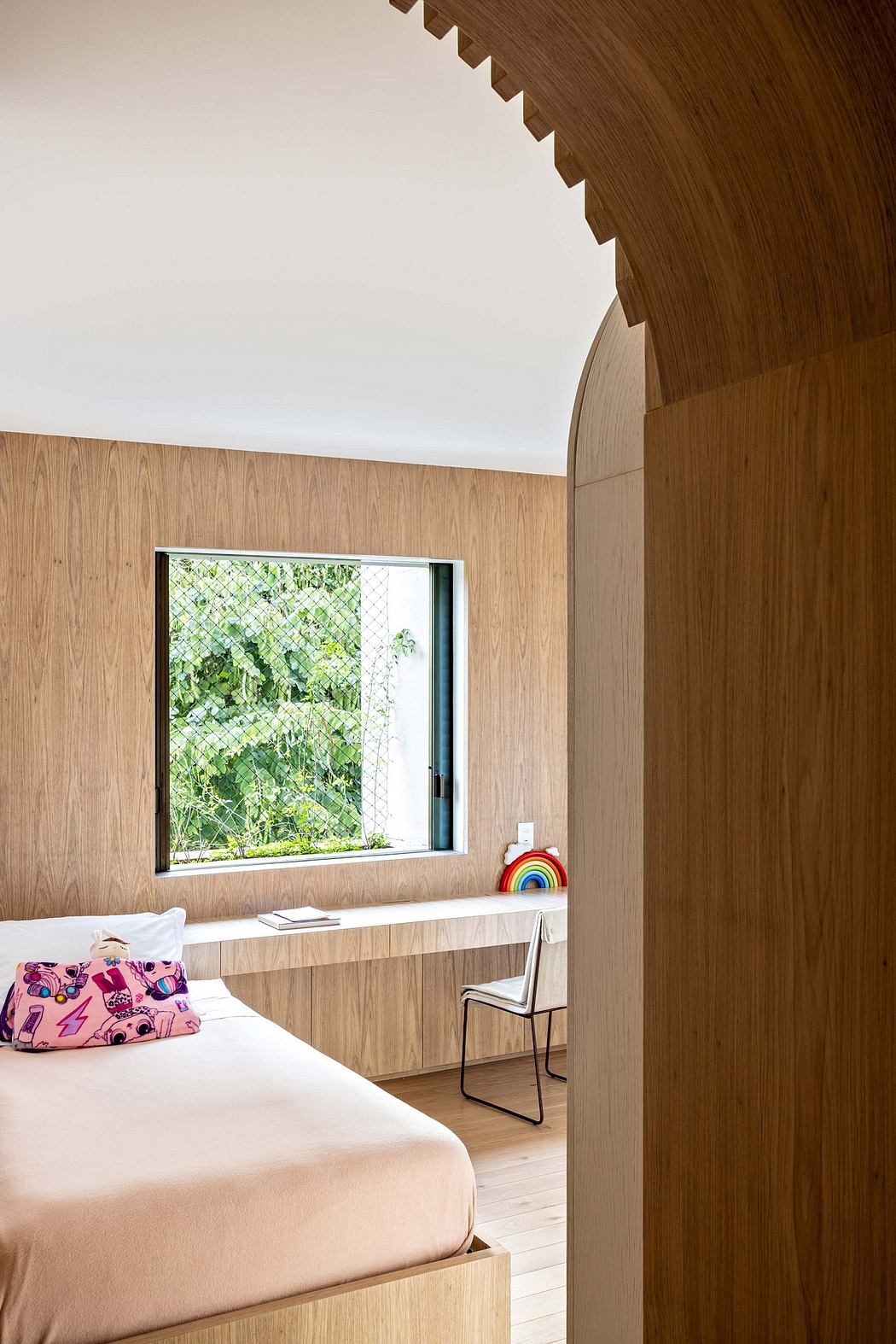 A modern bedroom with wooden walls, large window overlooking greenery, and minimalist decor.