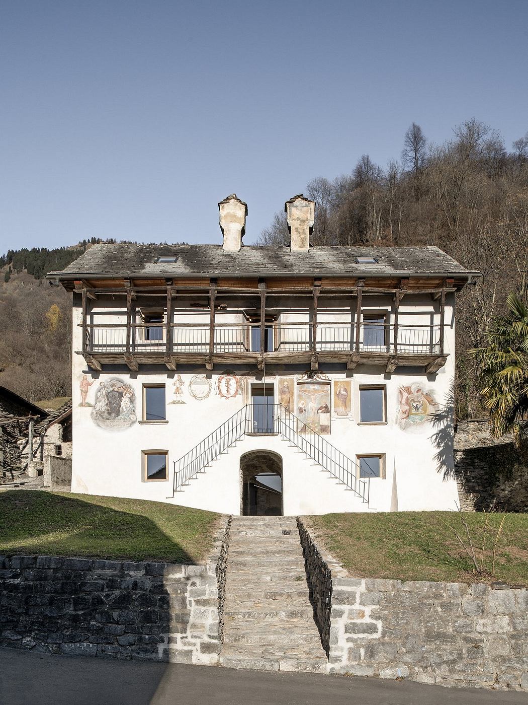 A three-story historic Alpine-style house with decorative archways, balconies, and frescoes.