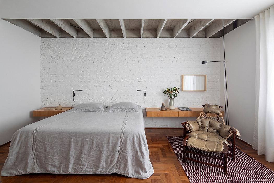 Minimalist bedroom with exposed concrete beams, brick wall, and wood flooring.
