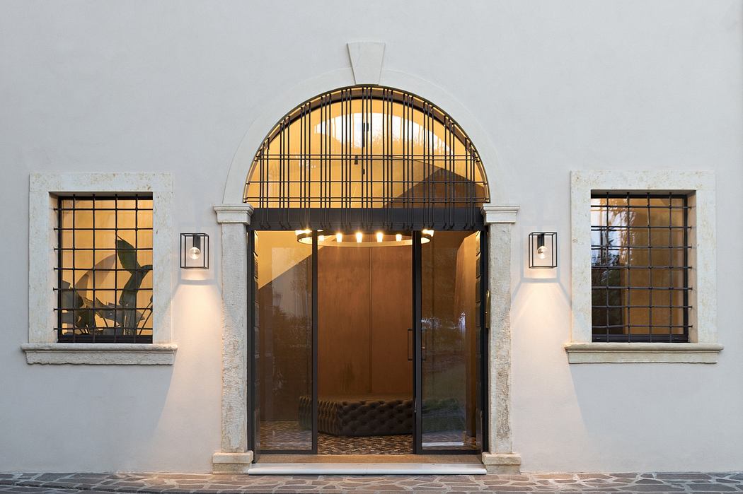 Ornate arched doorway with intricate metalwork framing a glass entry, flanked by windows.