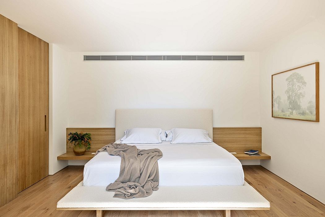 A minimalist bedroom with wood accents, a large bed, and a landscape painting on the wall.