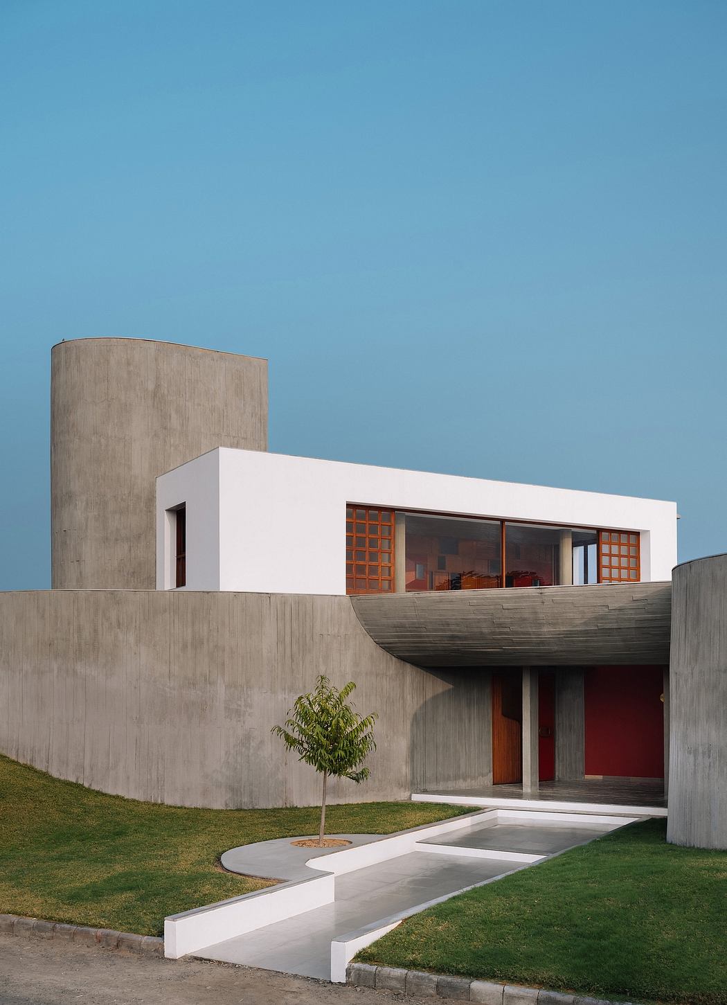 A modern, concrete and glass structure with a raised patio and a small tree in the foreground.