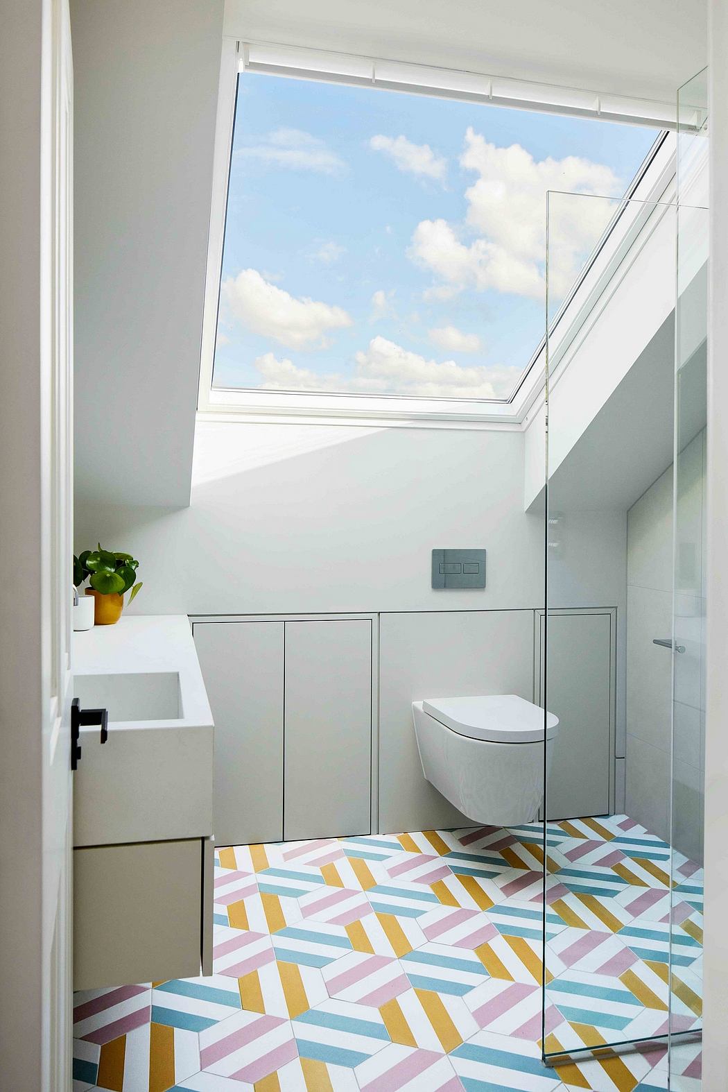 A bright, modern bathroom with a patterned tile floor and a large skylight window.