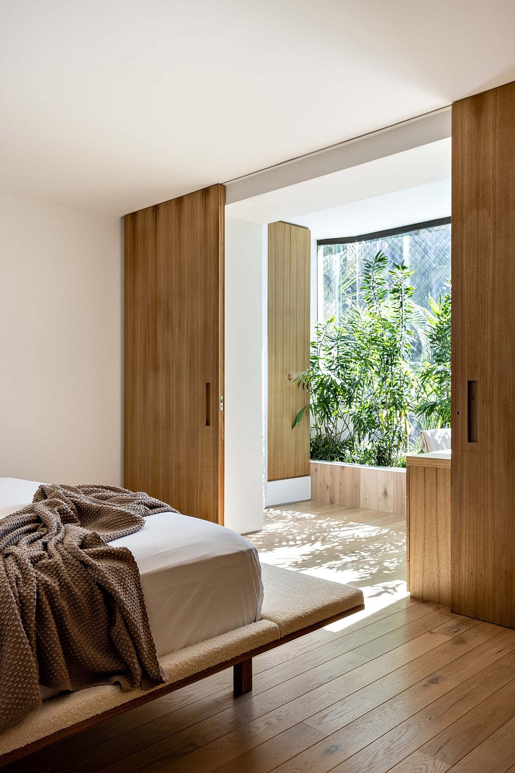 A cozy, modern bedroom with wooden paneling, a view to the greenery outside.