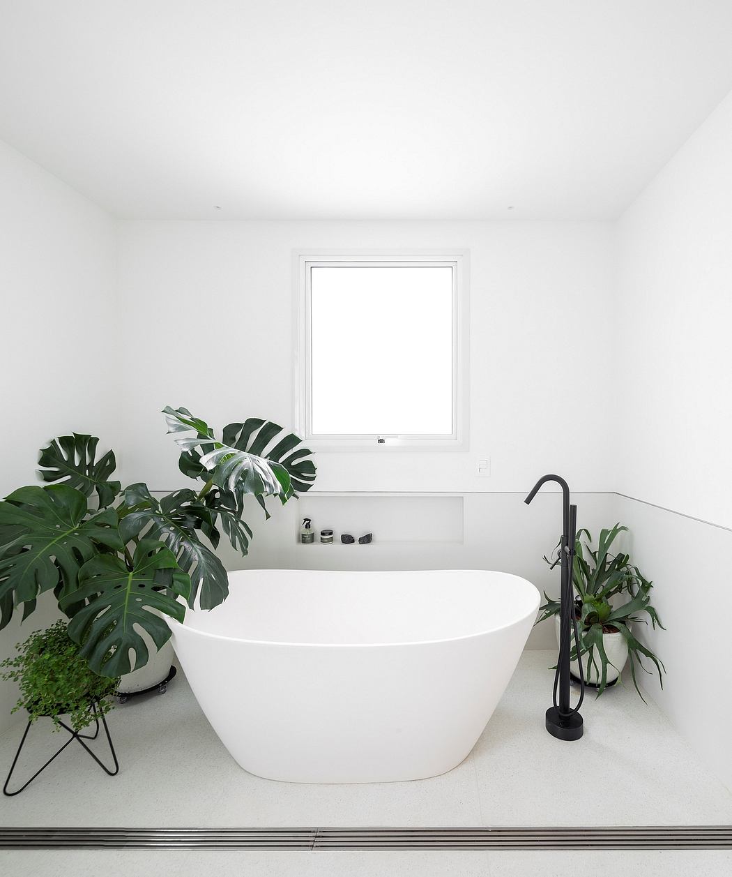 White modern bathtub, black faucet, large windows, lush green plants, minimalist design.