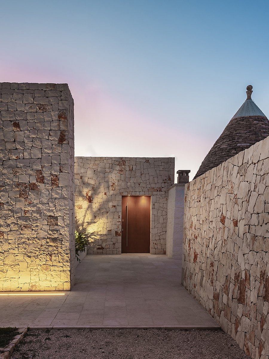 Striking exterior of a stone building with a domed roof and a wooden door, set against a colorful sky.