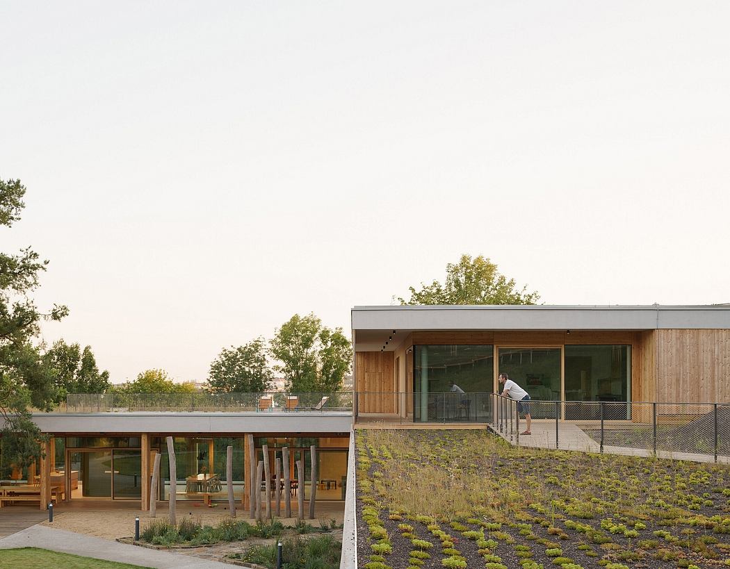 A modern, low-profile building with a wooden exterior and expansive glazing, set against a lush landscape.