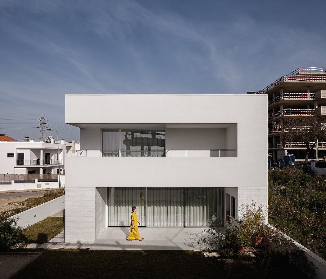 A modern white building with large windows and a person in yellow dress standing outside.
