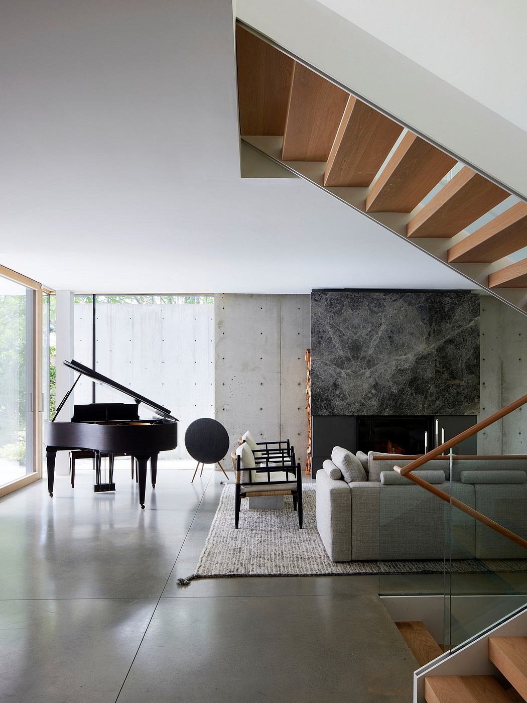 A contemporary living room with a grand piano, modern furnishings, and a sculptural wooden staircase.
