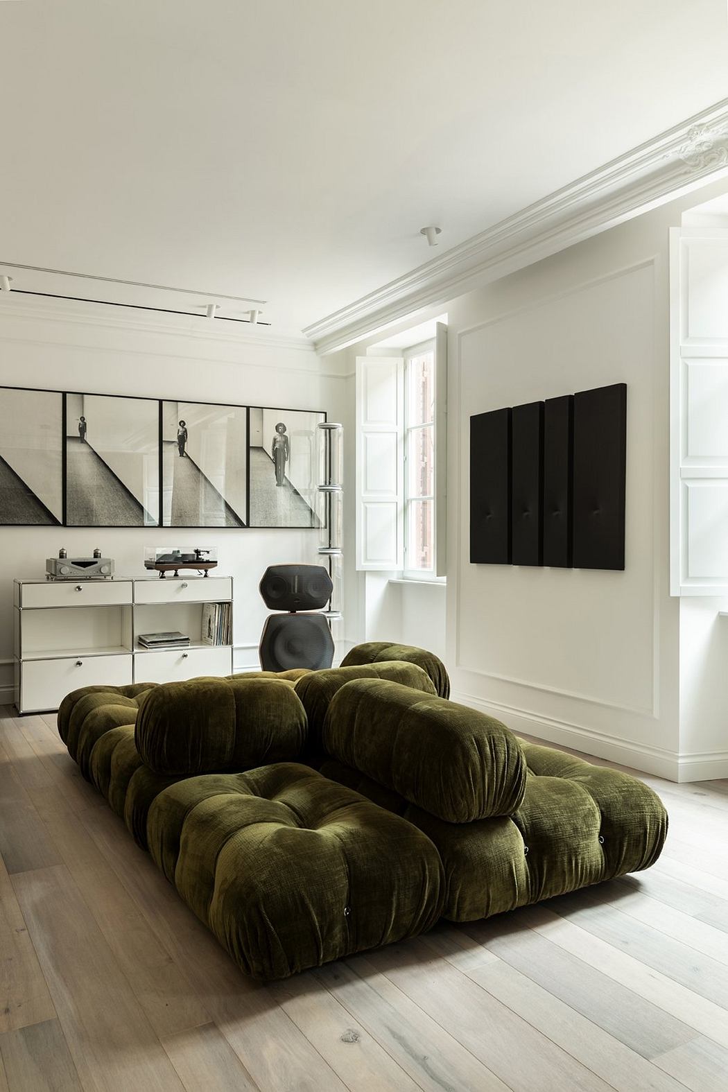 Minimalist living room with large, tufted green sofa and black and white art.