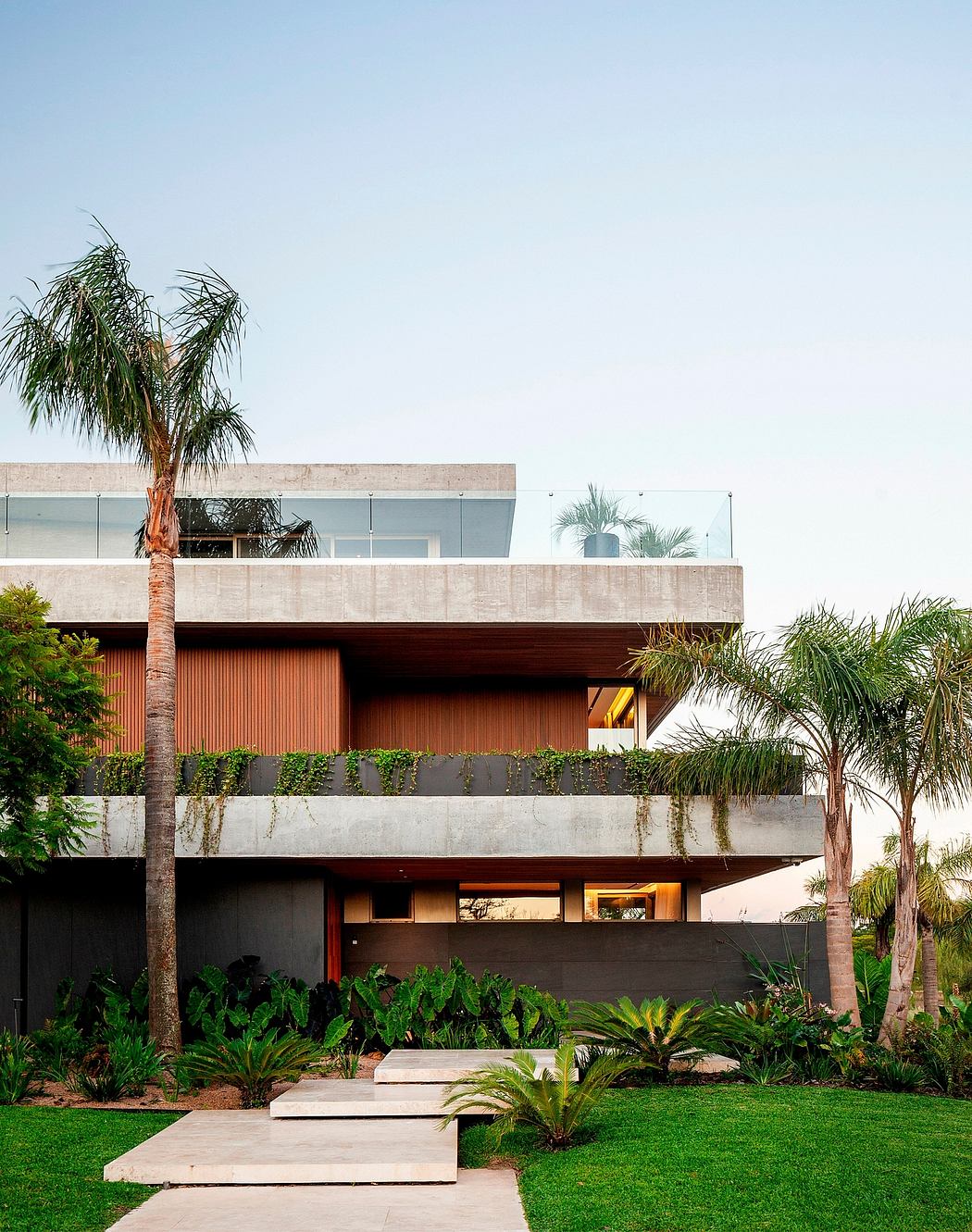 Modern tropical house with concrete walls, wooden accents, and lush greenery surrounding the entrance.
