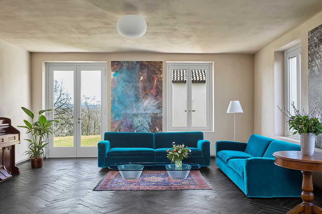 Spacious living room with large teal velvet sofas, colorful abstract artwork, and wooden floors.