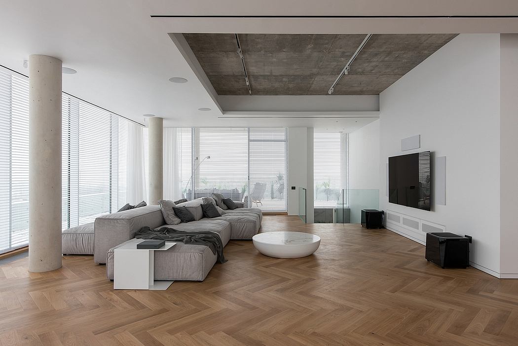Minimalist living room with concrete ceiling, wood floor, and glass walls overlooking nature.
