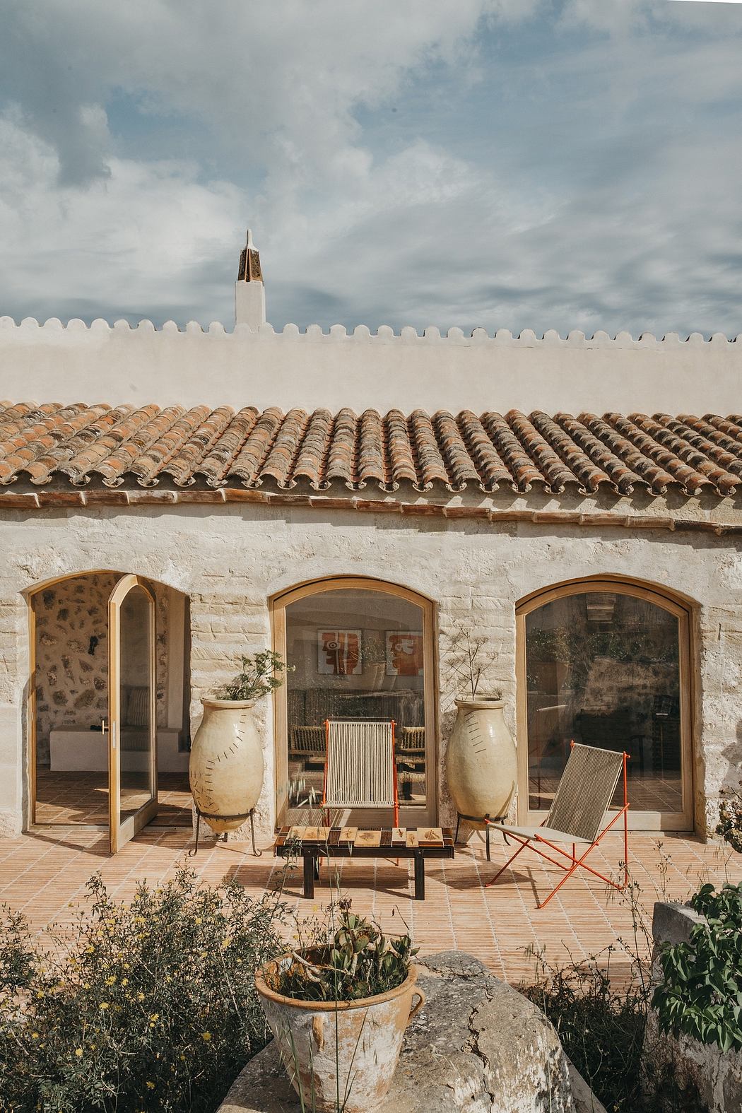 A rustic Mediterranean-style villa with arched windows, terracotta roofing, and potted plants.
